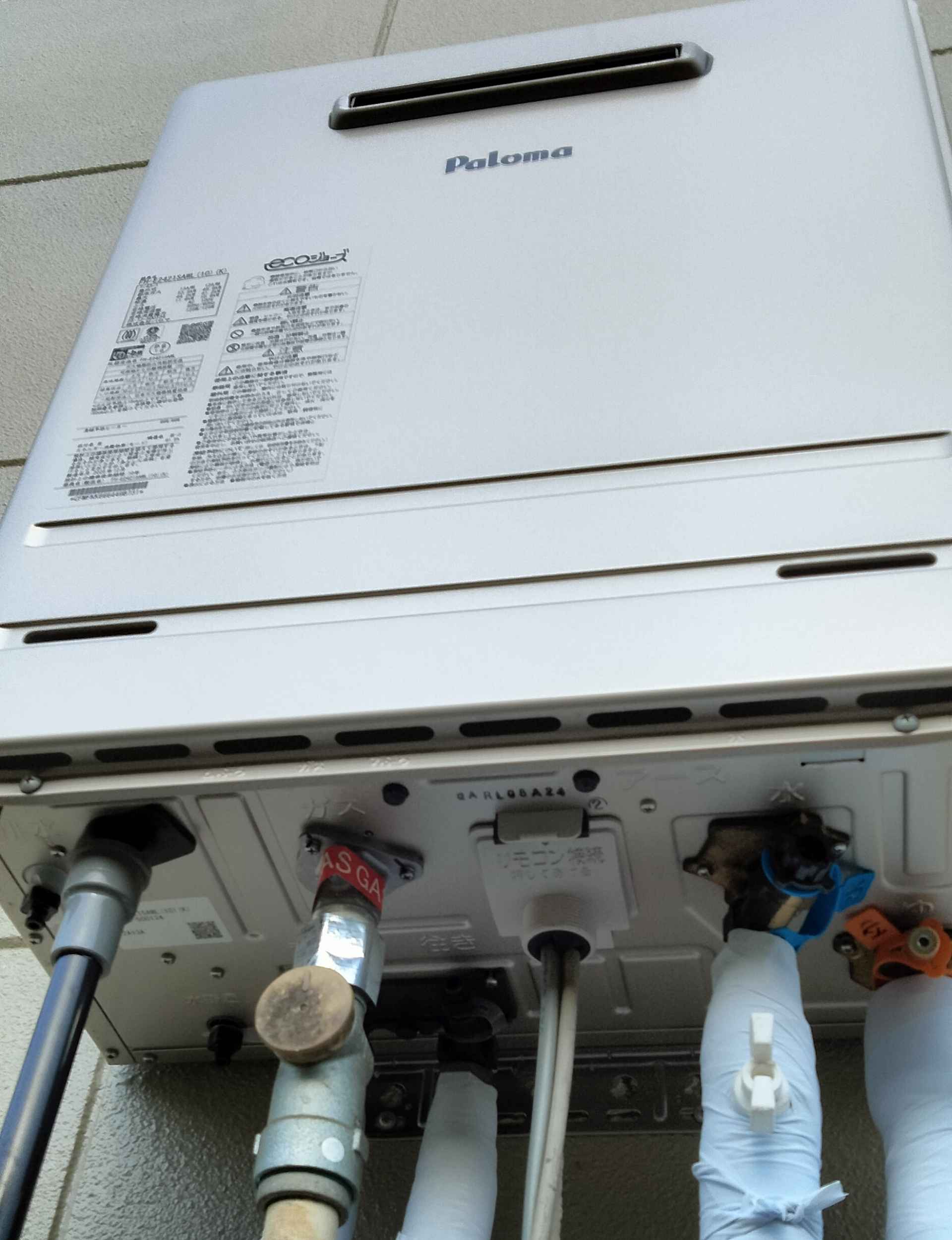 パロマのエコジョーズ給湯器FH-E2421を屋外壁掛け設置し下部の配管接続周りを見上げた様子